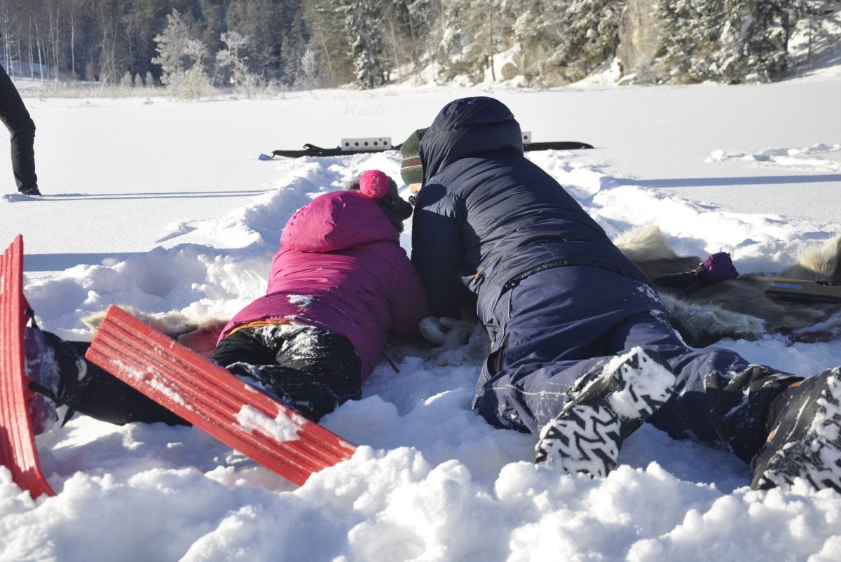 En jente og gutt ligger på magen i snøen og skyter på blink