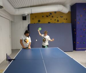 To energiske deltakere spiller bordtennis i gymsalen.