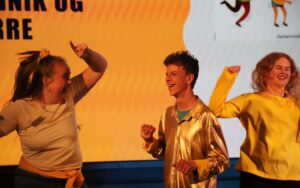 Glade mennesker danser og shower på scenen.