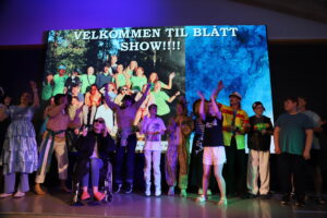 Blå gruppe på scenen, men teksten "Velkommen til blått show" bak