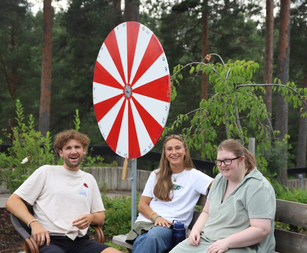 Tre, smilende mennesker, foran et lotteri-hjul.