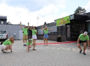 Tre mennesker danser, mens tre andre tegner med kritt på asfalten foran hovedinngangen.