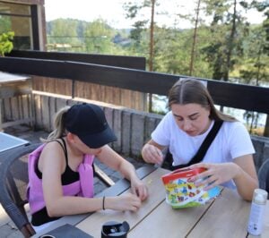To mennesker sitter konsentrert og lager perlearmbånd.