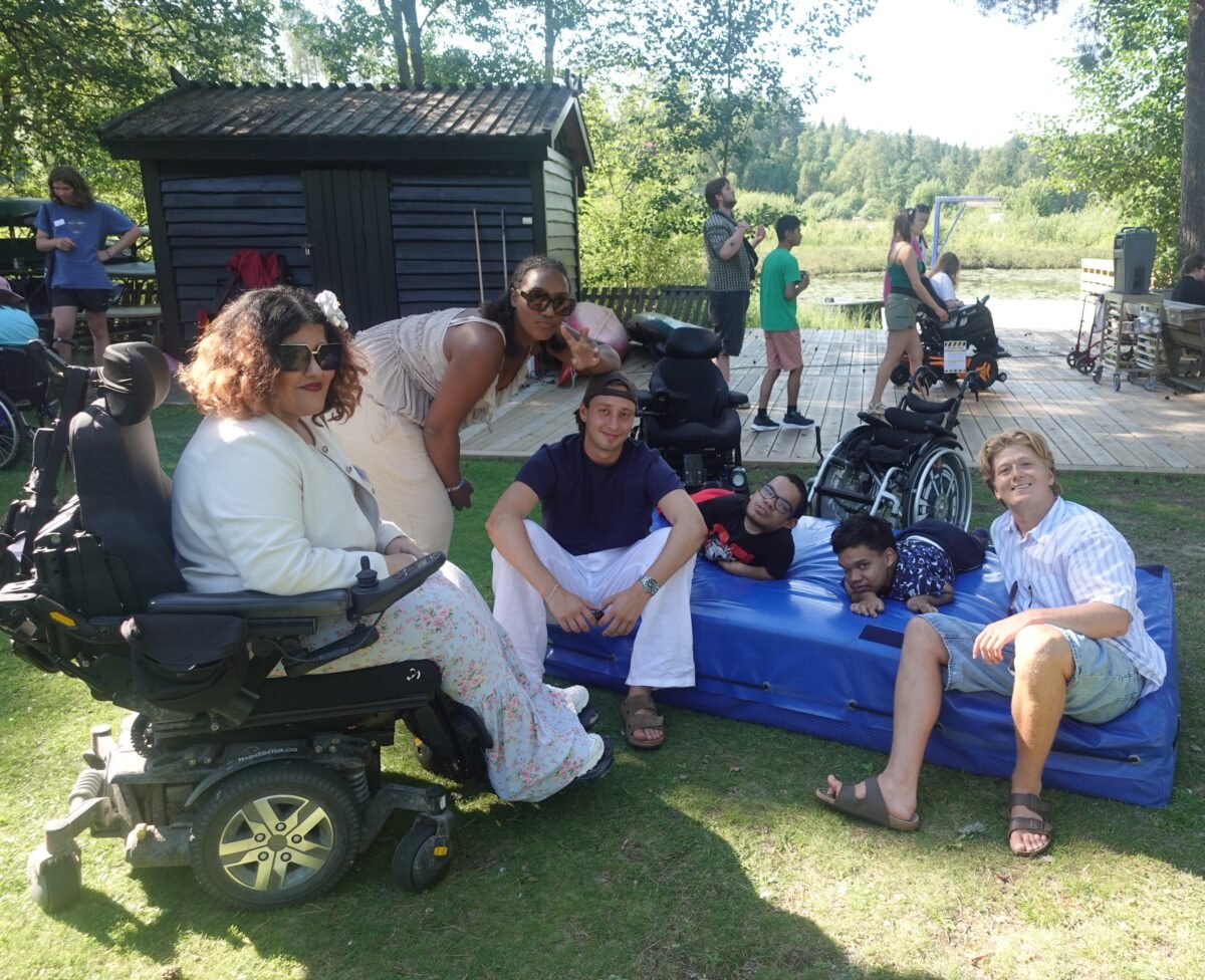 Gruppe mennesker slapper av på gress-sletta nede ved brygga.