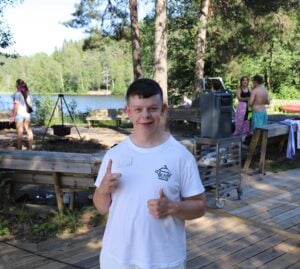 Gutt smiler mot kamera. Viser V-tegn og med den andre hånden, tommel opp.