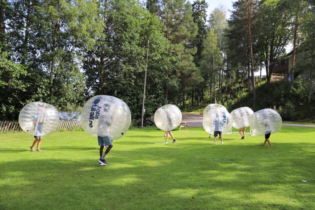 En gruppe løper rundt på gressletta med store badeballer rundt hodet.