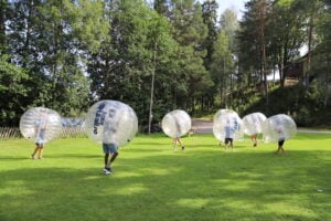 En gruppe løper rundt på gressletta med store badeballer rundt hodet.