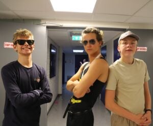 Tre karer står i gangen med solbriller, og tøffer seg for kameraet.