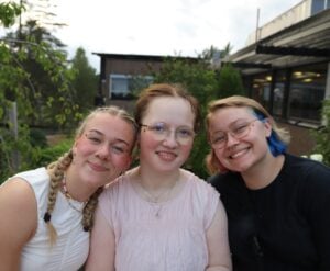 Tre jenter smiler og klemmer.