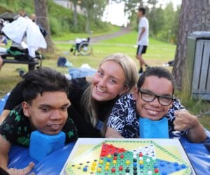 Tre mennesker smiler til kamera. De spiller kinasjakk.