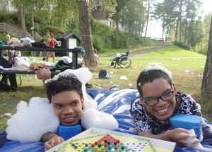 To mennesker ligger på en gresslette og smiler. De har masse badeskum på hodet.