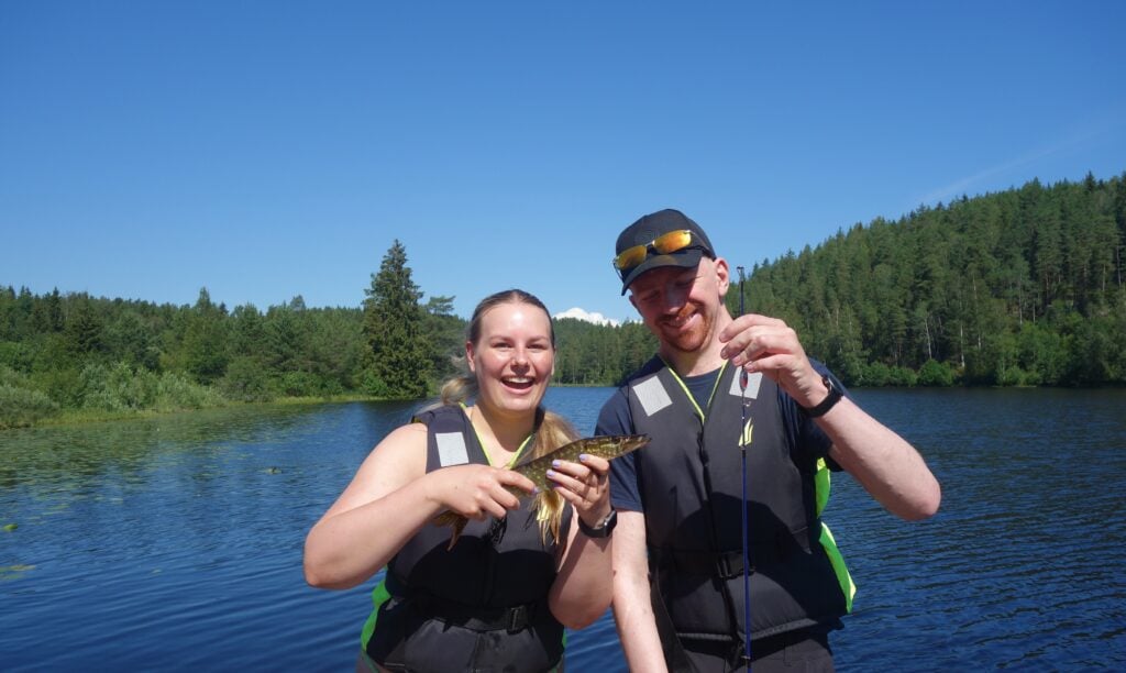 En glad ung dame og mann står på brygga og viser stolt frem en fisk de har fisket