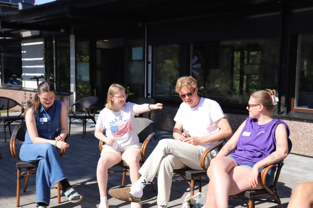Tre unge damer og en mann som sitter i atriet i solen