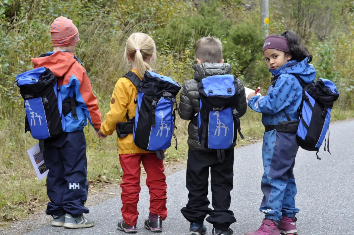 Foto av fire små barn som går på en gangvei med skolesekk på ryggen