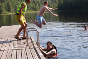 Badebrygge, sommer. Ung mann hopper i vannet.