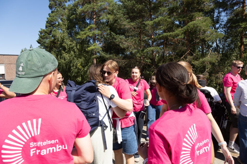 utendørs, unge menn og kvinner i rosa t-skjorter der det står Frambu på ryggen. De klemmer.
